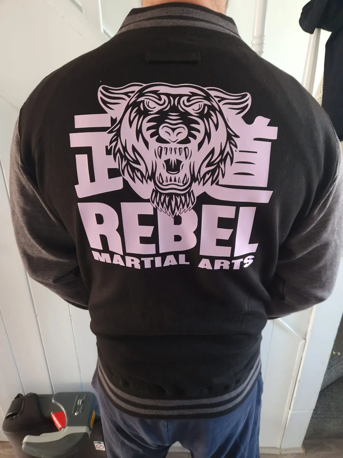 Rebel Martial Arts black varsity jacket worn to show the large back graphic